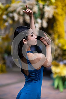 Close-up portrait of a beautiful Asian ballerina posing against the background of a building decorated with flowers.