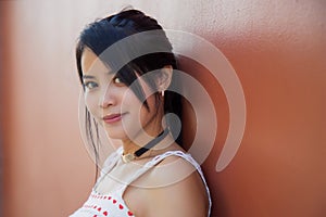 Close up portrait of beautiful Asian woman in a white dress with heart patterned looking at the camera next to an orange concrete