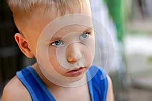 Close up portrait of beautiful baby boy with very serious look. Blond hair, blue eyes, strong emotions, sad face expression.