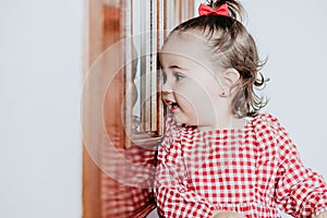 Close up portrait of beautiful baby girl at home looking by window door. One year old girl. Lifestyles indoor