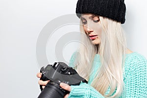 Close-up portrait of beautiful blonde girl photographer looking on DSLR camera, on white background.