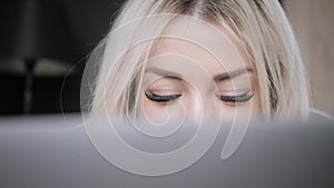 Close-up portrait of Beautiful blonde woman lying on the bed with gray aluminum laptop. Girl smiles, good mood. Blogging