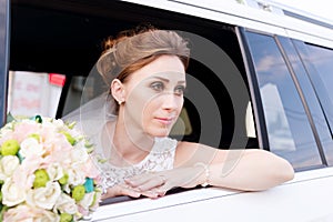 Close-up portrait of a beautiful bride aged beside her wedding bouquet in the window of a wedding car.