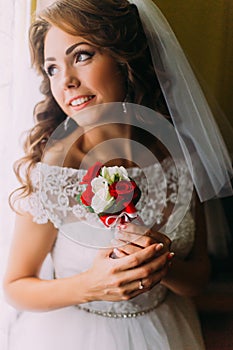 Close-up portrait of beautiful bride in wedding dress holding a cute bouquet with red and white roses dreaming her