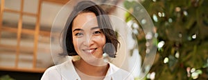 Close up portrait of beautiful brunette asian girl, smiling and looking flirty at camera, chuckle cute