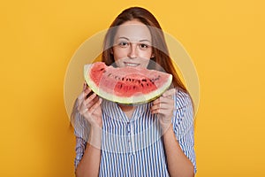 Close up portrait of beautiful brunette smiling young woman with slice of watermelon, charming lady wearing blouse posinhg