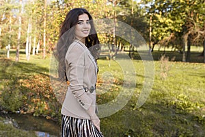 Close up portrait of a beautiful brunette teen girl with make up and in elegant fall outfit, posing in the park.