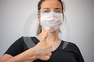Close up portrait of beautiful brunette young  woman wearing medical  mask and showing thumb up