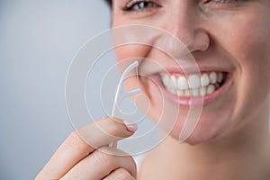 Close-up portrait of a beautiful caucasian woman with a flawless smile holding a toothpick with dental floss on a white