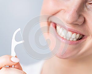 Close-up portrait of a beautiful caucasian woman with a flawless smile holding a toothpick with dental floss on a white