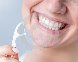 Close-up portrait of a beautiful caucasian woman with a flawless smile holding a toothpick with dental floss on a white