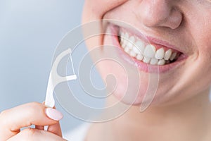 Close-up portrait of a beautiful caucasian woman with a flawless smile holding a toothpick with dental floss on a white