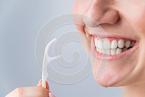 Close-up portrait of a beautiful caucasian woman with a flawless smile holding a toothpick with dental floss on a white