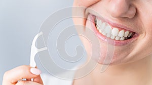 Close-up portrait of a beautiful caucasian woman with a flawless smile holding a toothpick with dental floss on a white