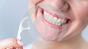 Close-up portrait of a beautiful caucasian woman with a flawless smile holding a toothpick with dental floss on a white