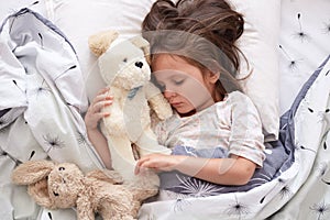 Close up portrait of beautiful cute little girl sleeping peacefully and hugging her stuffed toys in bed, charming kid with closed