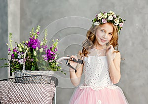 Close-up portrait of a beautiful cute little girl in a wreath of fresh flowers on her head and a basket of beautiful spring