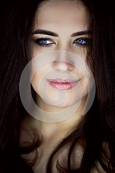 Close-up portrait of beautiful elegant brunette with long hair. In the eyes of the reflection of the lamp. Studio, dark