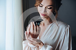 Close up portrait of a beautiful gentle bride in a beige peignoir with a butterfly with black and blue wings sits on the