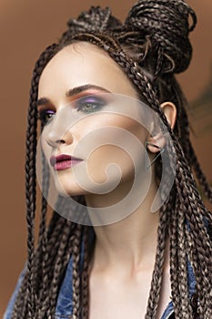 Close up portrait of a beautiful girl with an afro cornrows hairstyle, wearing a casual denim jacket, near to a palm tree leaves.