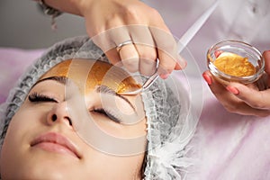 Close-up of portrait of beautiful girl applying gold facial mask