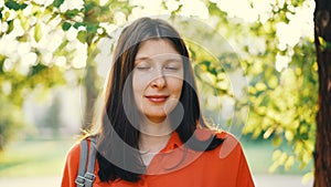 Close-up portrait of beautiful girl with brown hair looking at camera and smiling with summer park in background