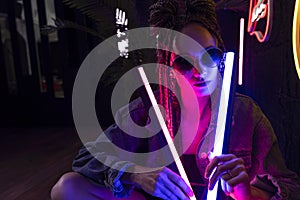 Close up portrait of a beautiful girl with an cornrows, wearing a denim jacket and sunglasses, holds in her hands neon night club