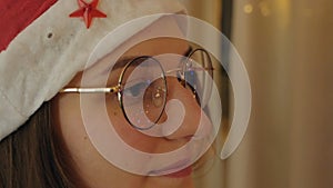 Close-up portrait of a beautiful girl in glasses looking at the Christmas lights. Reflection in glasses