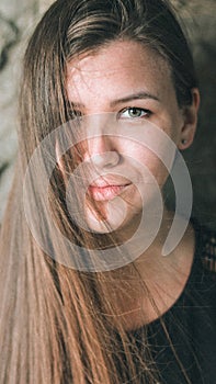 Close-up portrait of a beautiful girl with long flowing hair covering one eye. A young woman looks straight into the