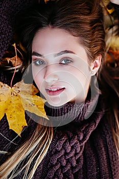 Close-up portrait of beautiful girl lying on fallen leaves of maple tree autumn