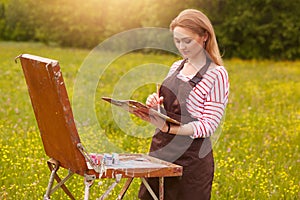 Close up portrait of beautiful girl with painting picture on easel in nature, young attractive woman involved in creativity and