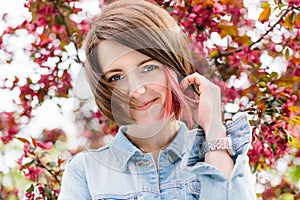 Close up portrait of a beautiful girl with pink hair standing in a blooming apple garden. Spring, outdoors.