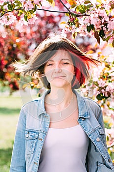 Close up portrait of a beautiful girl with pink hair standing in a blooming apple garden. Spring, outdoors.