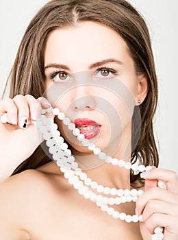 Close-up portrait of a beautiful girl with red lips, holding a pearl necklace. mouth open, pearls touches her lips. Red