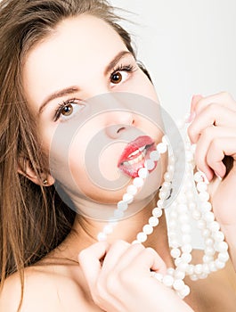 Close-up portrait of a beautiful girl with red lips, holding a pearl necklace. mouth open, pearls touches her lips. Red