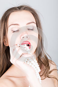 Close-up portrait of a beautiful girl with red lips, holding a pearl necklace. mouth open, pearls touches her lips. Red