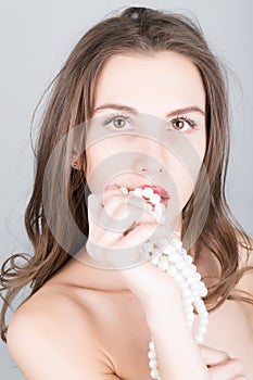 Close-up portrait of a beautiful girl with red lips, holding a pearl necklace. mouth open, pearls touches her lips. Red