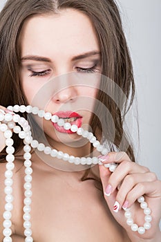 Close-up portrait of a beautiful girl with red lips, holding a pearl necklace. mouth open, pearls touches her lips. Red