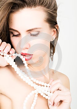 Close-up portrait of a beautiful girl with red lips, holding a pearl necklace. mouth open, pearls touches her lips. Red