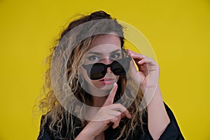 Close-up portrait beautiful girl on a yellow background. woman showing finger silence, girl showing shh sign keep secret