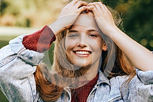 Close-up portrait of beautiful happy young woman smiling broadly with healthy toothy smile, wearing red sweater and denim jacket,