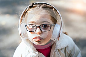 Close up portrait of beautiful little girl in eyeglasses with down syndrome smiling and looking into camera with
