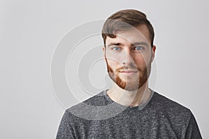 Close up portrait of beautiful manly bearded guy with stylish hairstyle smiling, looking in camera with happy and calm