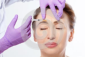 Close-up portrait of a beautiful middle age woman and doctor hands making botox injection isolated on white background. Collagen.