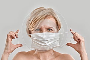 Close up portrait of beautiful middle aged woman holding white medical mask near her face and looking at camera isolated