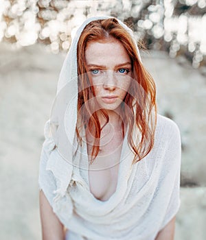 Close up portrait of a beautiful red haired girl in white medieval dress on glowing sun. Fairy tale story about brave heart woman photo