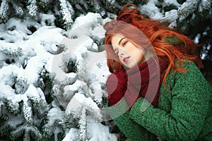 Close up portrait of a beautiful red-haired girl leaning on snowy fir tree bough with dreaming look.