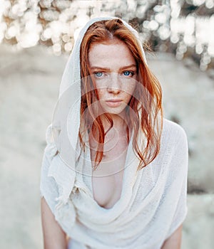 Close up portrait of a beautiful red haired girl in white medieval dress on glowing sun. Fairy tale story about brave heart woman