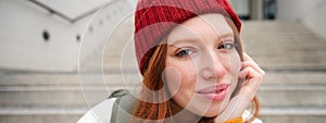 Close up portrait of beautiful redhead girl in red hat, urban woman with freckles and ginger hair, sits on stairs on