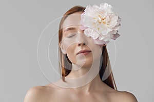 Close-up portrait of beautiful redheaded woman in lingerie with flower isolated over gray studio back ground. Fitness